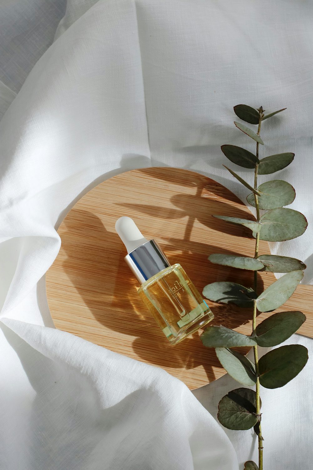 Halden facial serum in a glass dropper bottle on a bamboo board with eucalyptus